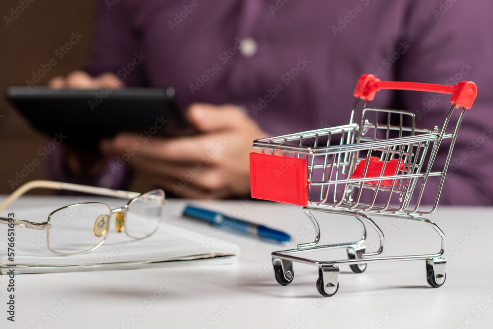 Man calculates the budget. Shopping cart a on table with calculator and paper. Man calculates the budget. Shopping cart a on table with calculator and paper.