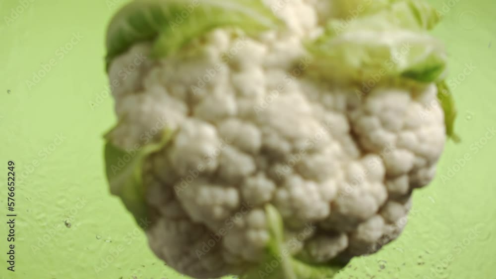 Slow motion of cauliflower falling into water surface on green background Slow motion of cauliflower falling into water surface on green background