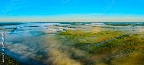 Aerial  view of a beautiful summer  landscape with a fog while dawn.  Photo from drone of a foggy landscape in spring. Top view to land while sunrise. Sun is above the horizon. Panorama.