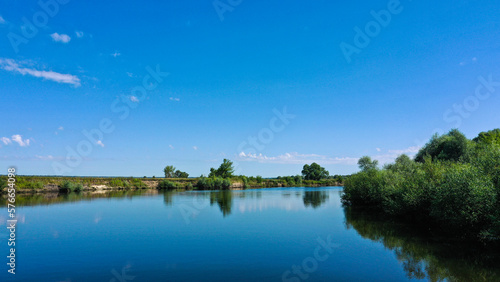 Aerial view of a beautiful summer landscape over river while dawn. Top view over river with a smooth water surface reflecting blue sky.