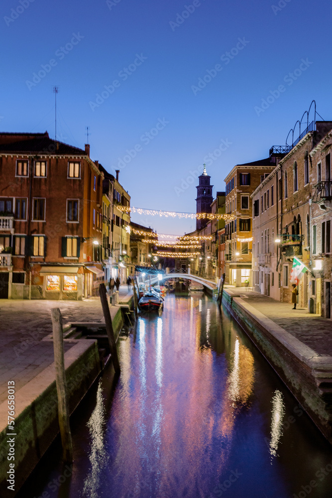 Venice at night. The canal flows between the houses, the water shimmers darkly and the occasional boat sails across it.