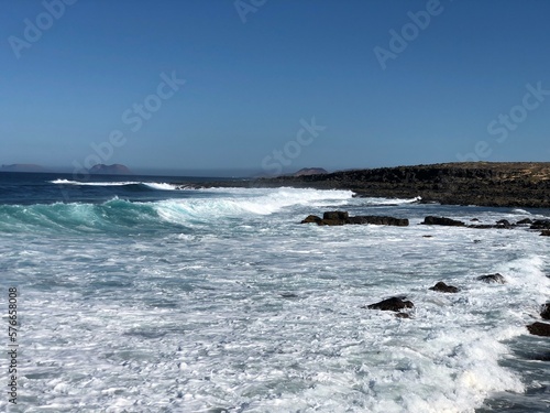 Ocean view background. Water splash from waves on rocky beach. Lanzarote island horizontal wallpaper.