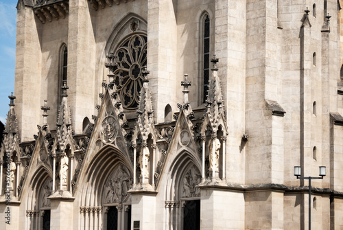 Diagonal aspect of the front of St Wenceslas Cathedral in Olomouc, Czechia, with tops of main entrance visible underneath columns, ornate white stonework and round window
