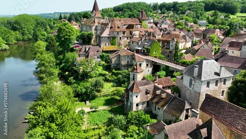 Small, medieval village situated next to a river, flowing through a rich forest in the heart of France. Droneshot flies over the village, showing medieval brick buildings, and walls overgrown by ivy. photo
