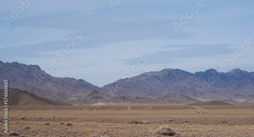 Rocky desert landscape with sparse vegetation and mountains peaks in a blue haze. Typical landscape near at Nepal Tibet border. Flat dry desert with mountains.