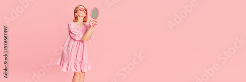 Beauty as it is. Young tender girl in pink dress looking at mirror over pink studio background. Concept of beauty, emotions, fashion, lifestyle and youth culture. Banner. Copy space for ad