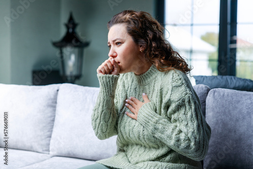 Sick woman sitting on sofa and having cough photo