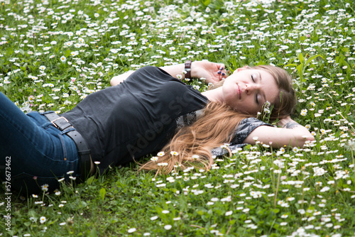 smiling young woman lying on a lawn with daisies in summer field © Alevtina