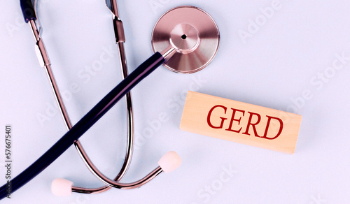 On a blue background, a stethoscope and wooden block with the word GERD .Medical concept