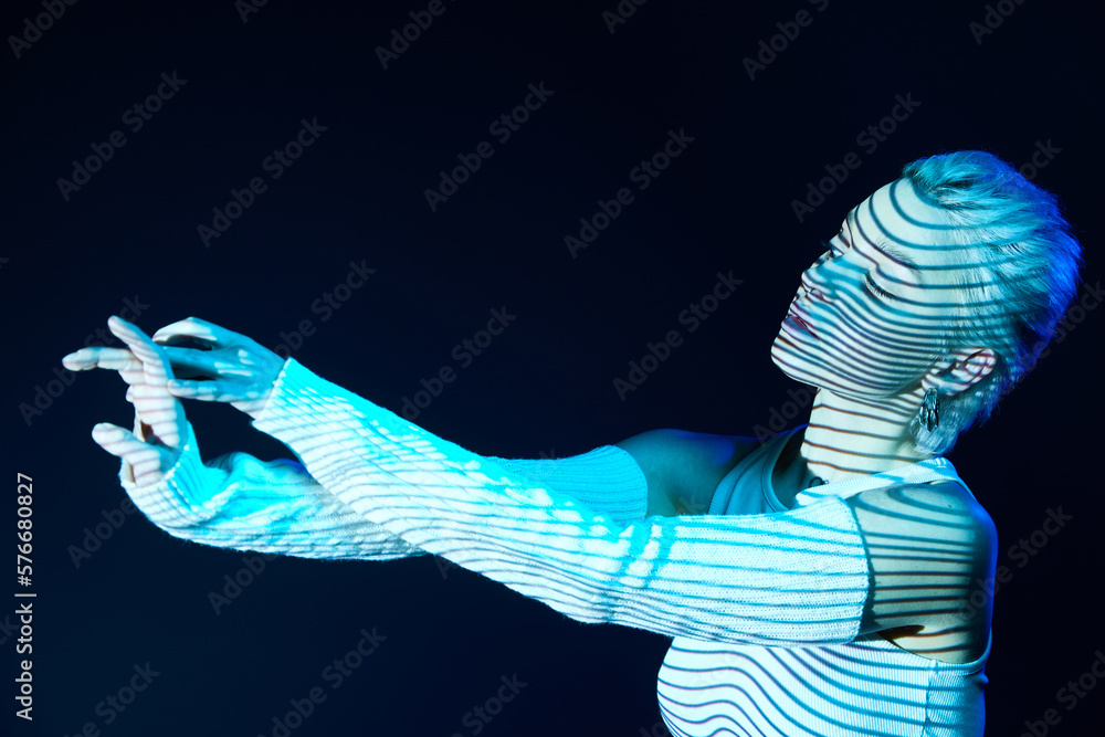 Fototapeta premium Virtual reality. Portrait of young blonde girl with neon stripes on face posing over dark background in blue neon lights. Concept of art, modern style, cyberpunk, futurism and creativity