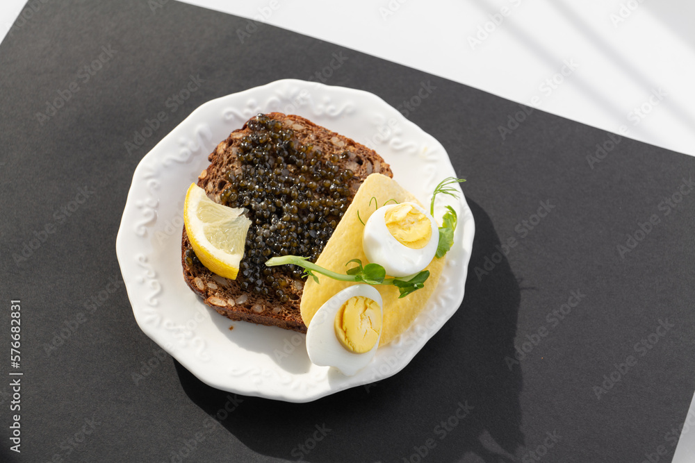 Black caviar on a sandwich with eggs, lemon, greenery