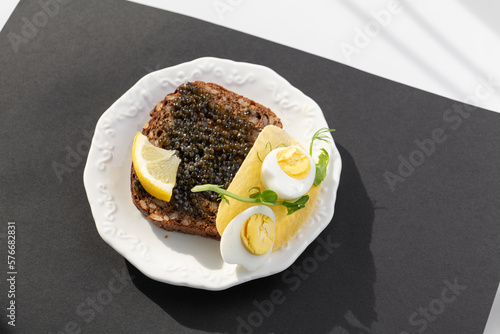 Obraz na płótnie Black caviar on a sandwich with eggs, lemon, greenery w salonie