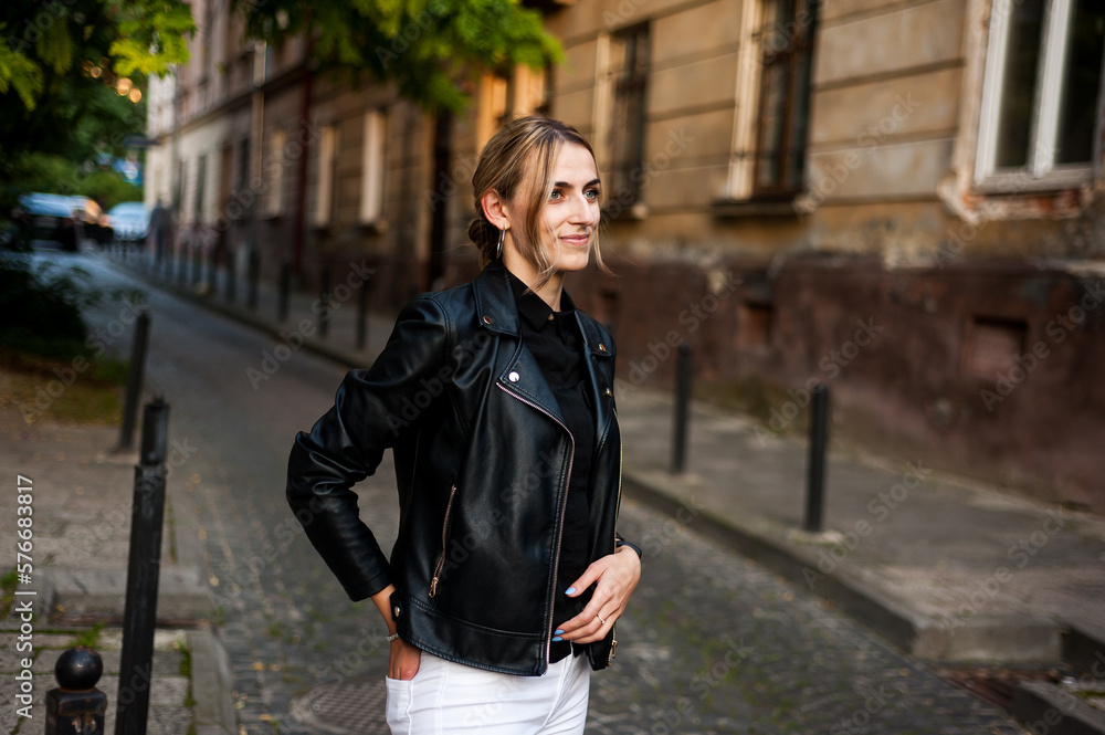 Smiling woman in the city street wearing black leather jacket and white pants and sunglasses
