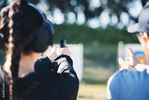 Woman, gun and learning to shoot outdoor with instructor at shooting range for target training. Safety and security with hand teaching person sport game or aim with gear and firearm for focus photo