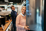 Middle aged couple, satisfied customers choosing fridge in appliances store.