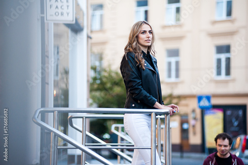 Smiling woman in the city street wearing black leather jacket and white pants