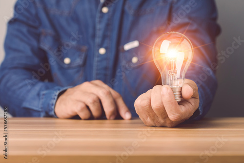 Close up Businessman holding a clear light bulb with light effect on gray space wall background. Concept of new ideas for work.