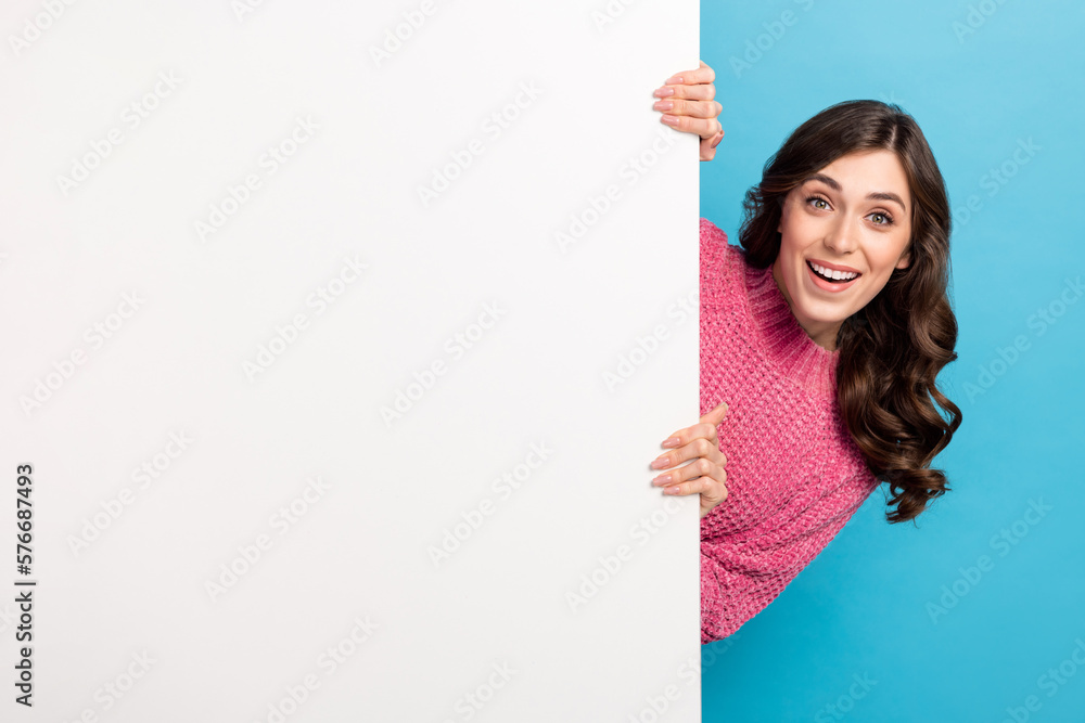Photo of young playful promoter lady hiding behind huge billboard empty space advertisement crazy proposition isolated on blue color background Photo of young playful promoter lady hiding behind huge billboard empty space advertisement crazy proposition isolated on blue color background
