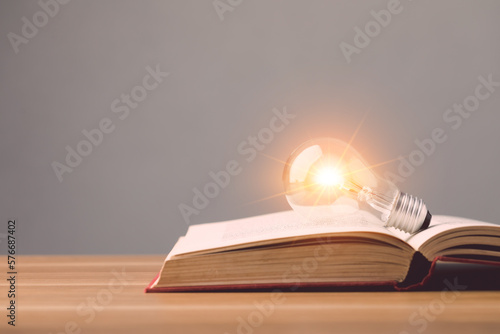 Canvas Print Clear light bulb with light effect on old book and put on wooden desk with grey space wall background