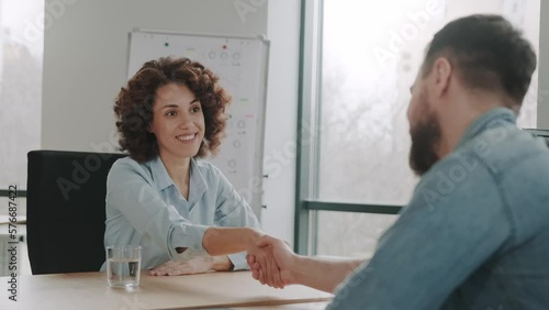 Excited young African American female woman shake hand of male recruiter or employer at office meeting. Happy diverse business partners handshakes after a successful job interview.