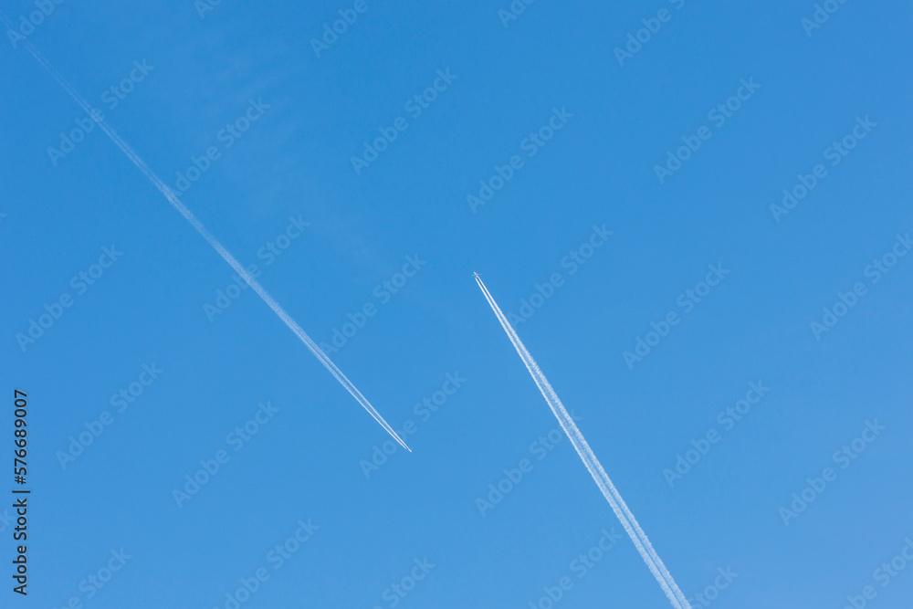 Two planes with white contrail meet head-on in blue sky Two planes with white contrail meet head-on in blue sky