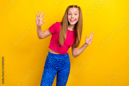 Photo of optimistic cute schoolgirl with straight hairstyle wear pink t-shirt dancing showing hands isolated on yellow color background