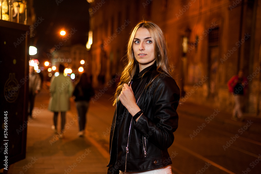 Fototapeta premium Beautiful smiling woman in leather black jacket in the night city.