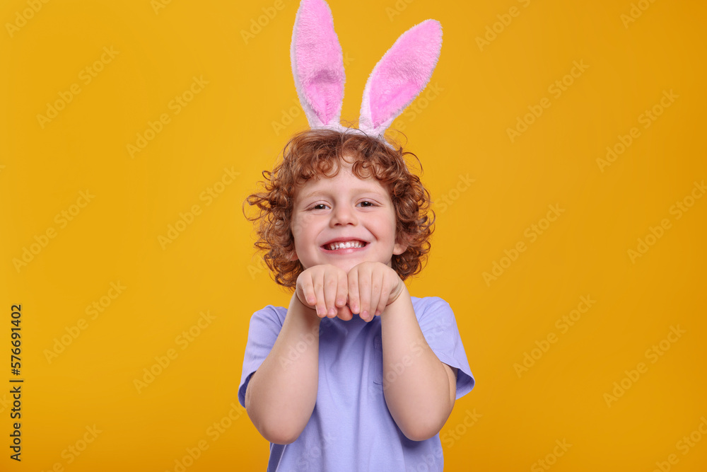 Portrait of happy boy wearing cute bunny ears headband on orange background. Easter celebration