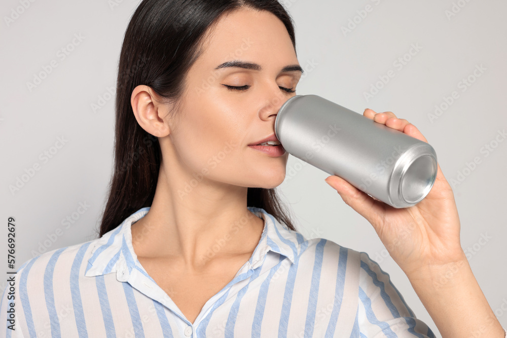 Beautiful young woman drinking from tin can on light grey background, closeup Beautiful young woman drinking from tin can on light grey background, closeup