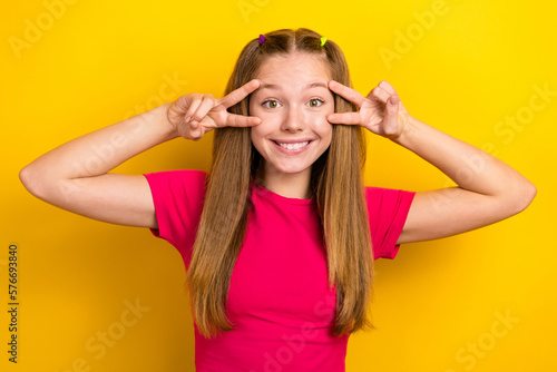 Portrait photo of young smiling cheerful teenager girl wearing pink t-shirt face v-sign peace symbols blogger isolated on yellow color background