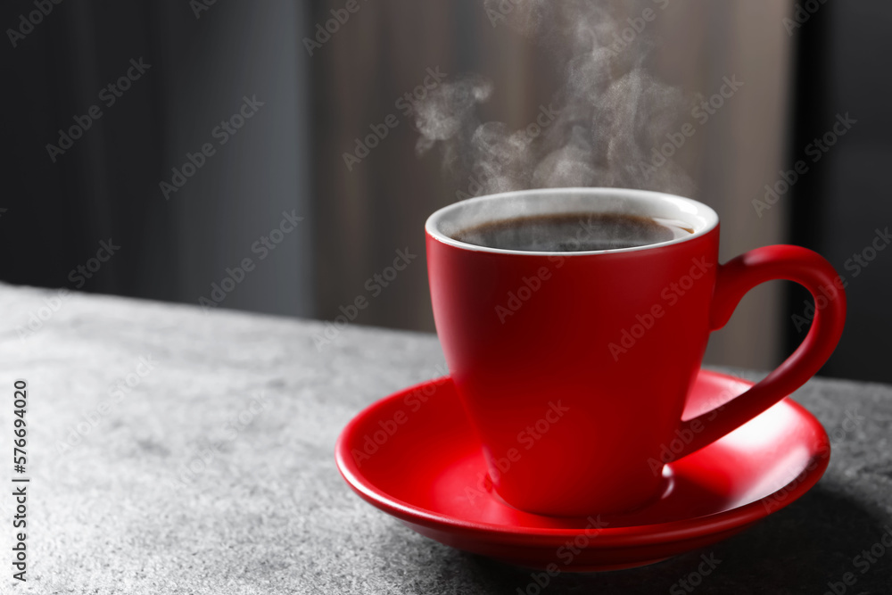 Red cup with hot steaming coffee on grey table indoors, space for text