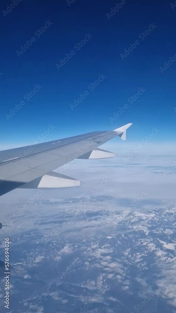 Plane flight above the Carpathian Mountains snowy peaks. Blue skyline and airplane wing seen through the window, vertical orientation Plane flight above the Carpathian Mountains snowy peaks. Blue skyline and airplane wing seen through the window, vertical orientation