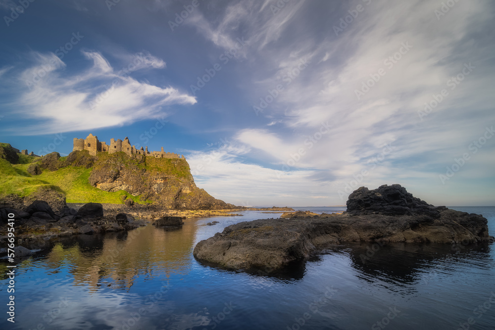 Dunluce Castle reflected in ocean, nested on the edge of cliff, part of Wild Atlantic Way, Northern Ireland. Filming location of popular TV show Game of Thrones