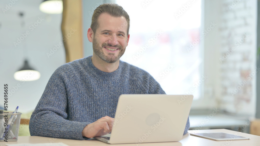 Middle Aged Man Smiling at Camera while using Laptop Middle Aged Man Smiling at Camera while using Laptop