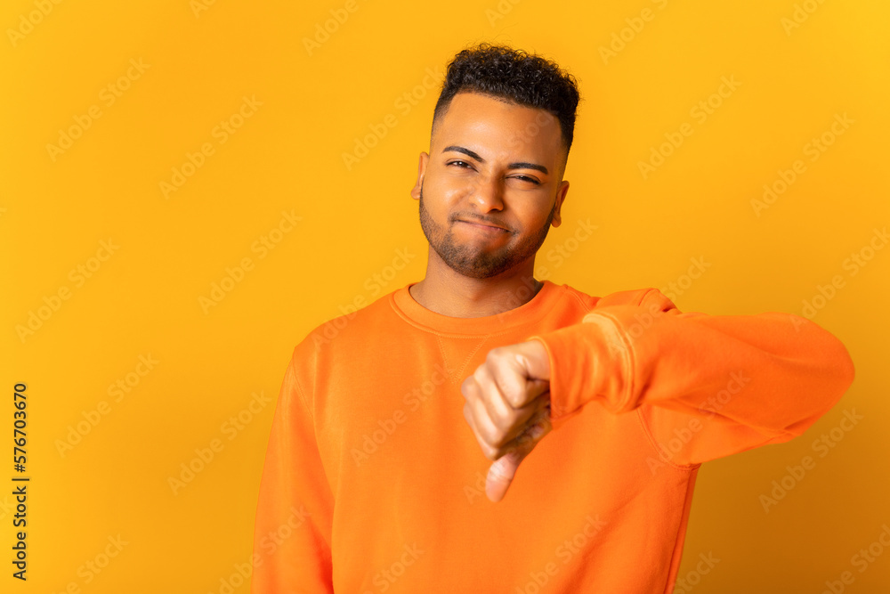 Dissatisfied young guy showing finger down gesture and feeling unhappy isolated on yellow background. Sad man dislike gesture Dissatisfied young guy showing finger down gesture and feeling unhappy isolated on yellow background. Sad man dislike gesture