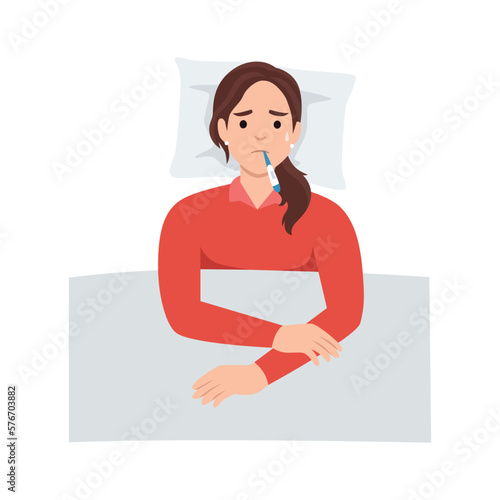 Woman suffering from flu in bed under blanket. She has fever and take thermometer in mouth with tissue paper and medicine on bed. Flu or cold allergy symptom