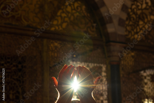 Islamic background photo. Muslim man praying with hands and direct sunlight photo