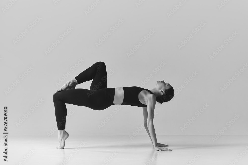 Balance. Black and white photography. Young slim, fit girl training, doing stretching exercises over studio background. Concept of sport, body care, beauty, fitness, active lifestyle. Ad Balance. Black and white photography. Young slim, fit girl training, doing stretching exercises over studio background. Concept of sport, body care, beauty, fitness, active lifestyle. Ad