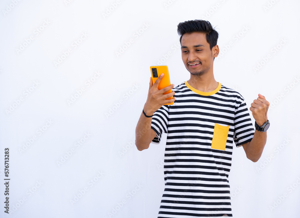 Indian Boy making joy Expressions while looking at mobile phone, Boy Holding a Unique Yellow mobile In front of him Indian Boy making joy Expressions while looking at mobile phone, Boy Holding a Unique Yellow mobile In front of him