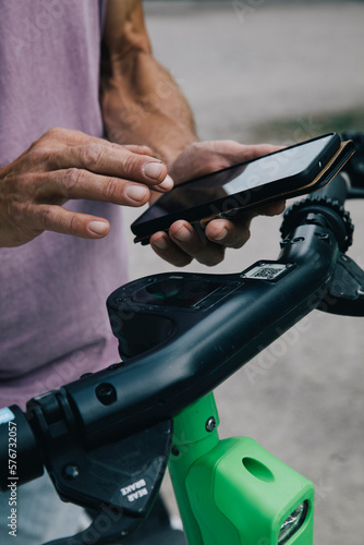 Close-up of hands using smart phon to unlock electric push scooter