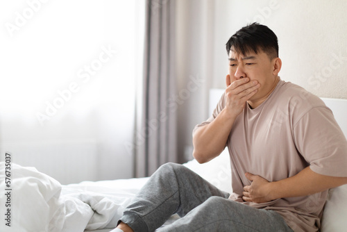 Photography Sick korean man sitting in bed, covering mouth, touching belly