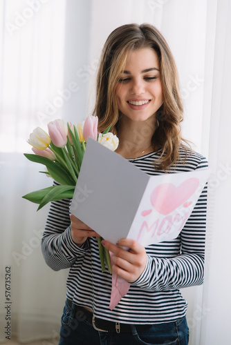 Happy Mother's day. Beautiful woman reading pastcard from her daughter and holding tulips. photo