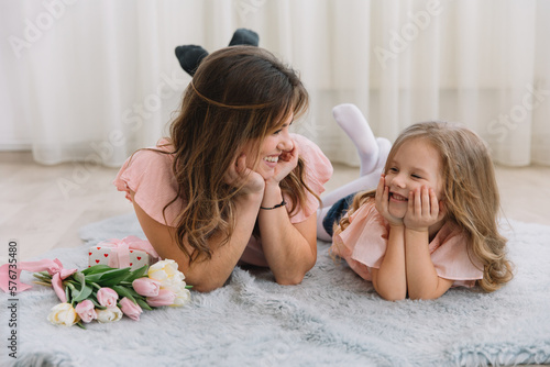 Happy mother's day. Child daughter congratulates mom and gives her flowers tulips and gift. Mum and girl smiling and hugging. Family holiday and togetherness. #576735480