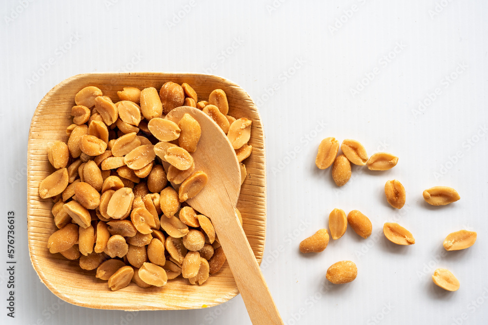 Roasted unsalted peanuts, are served in a biodegradable palm leaf tray and a spoon on a white background. Roasted unsalted peanuts, are served in a biodegradable palm leaf tray and a spoon on a white background.