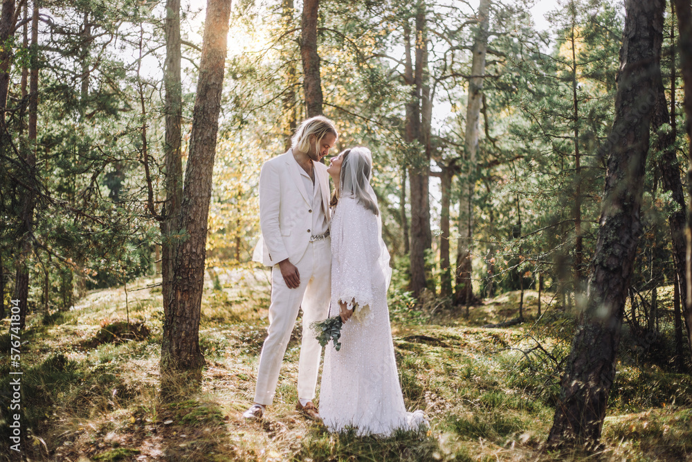 Bride looking at groom while standing amidst trees in forest on wedding day Bride looking at groom while standing amidst trees in forest on wedding day