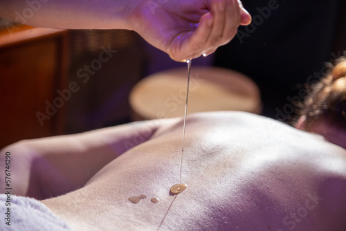 Detalhe do terapeuta derramando óleo nas costas de uma paciente que está deitada em uma maca. photo