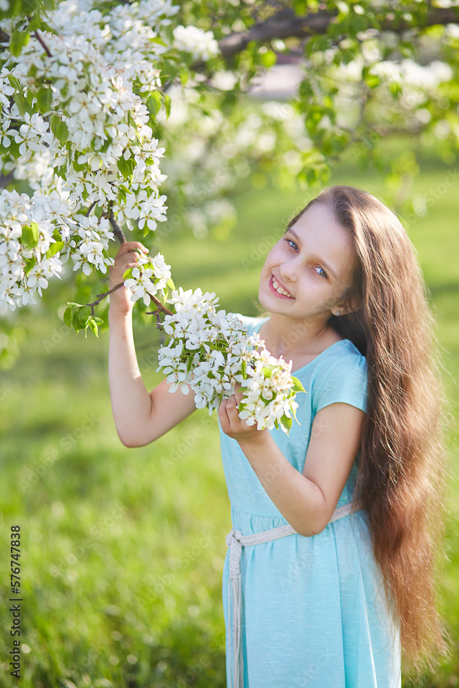 A young girl with loose long hair in a blooming apple orchard. Vertical orientation