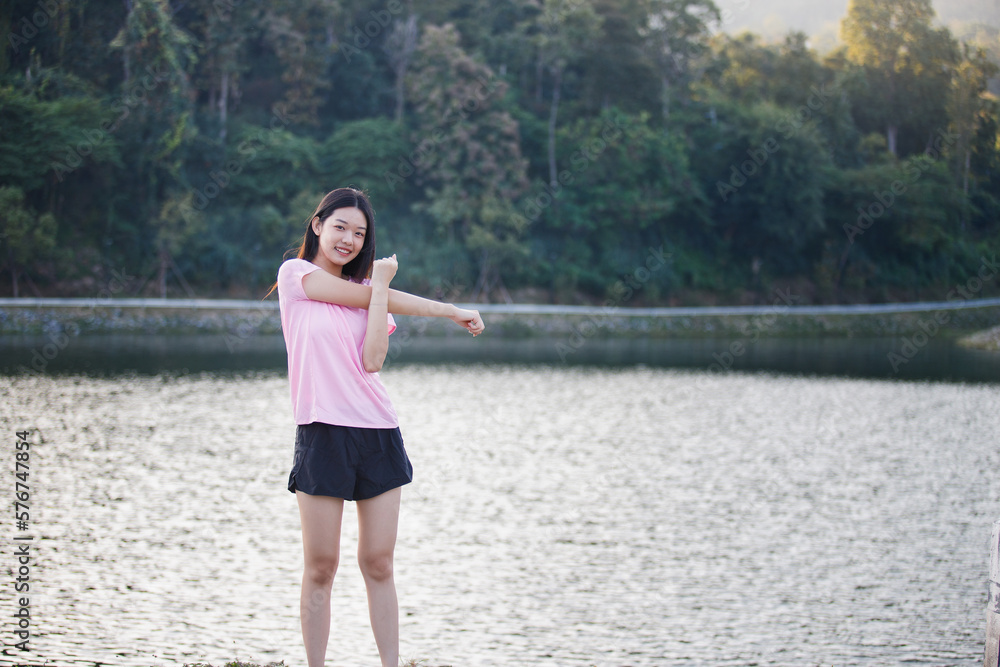 Attractive sports woman stretching arms preparing for morning workout near reservoir in park. Cardio workout or running jogging at nature park. Healthy lifestyle and wellness concept. Attractive sports woman stretching arms preparing for morning workout near reservoir in park. Cardio workout or running jogging at nature park. Healthy lifestyle and wellness concept.