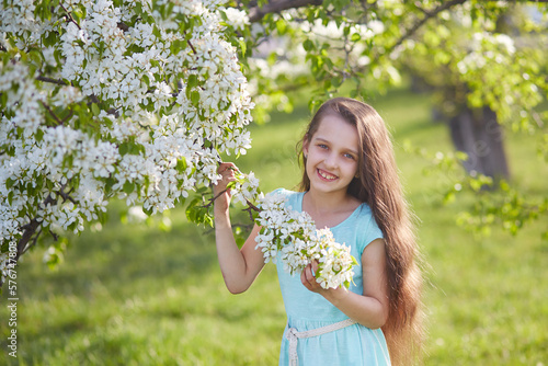 A smiling young girl in a blooming apple orchard. Beautiful spring background.