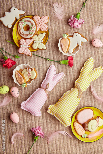 Fototapeta Naklejka Na Ścianę i Meble -  Aesthetic spring Easter background flat lay. Glazing Easter cookies, handmade bunny toys, pink flowers with feathers.